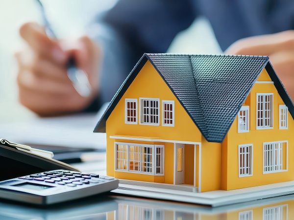 Roofing Estimate - DownUnder Roofing.com A person using a calculator to estimate the real estate property value, with a miniature house model on the desk and documents in front of them